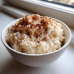 Close-up of creamy rice pudding in a white bowl, generously sprinkled with cinnamon.