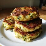 A stack of three golden-brown, crispy mashed potato cakes flecked with green chives on a white plate.
