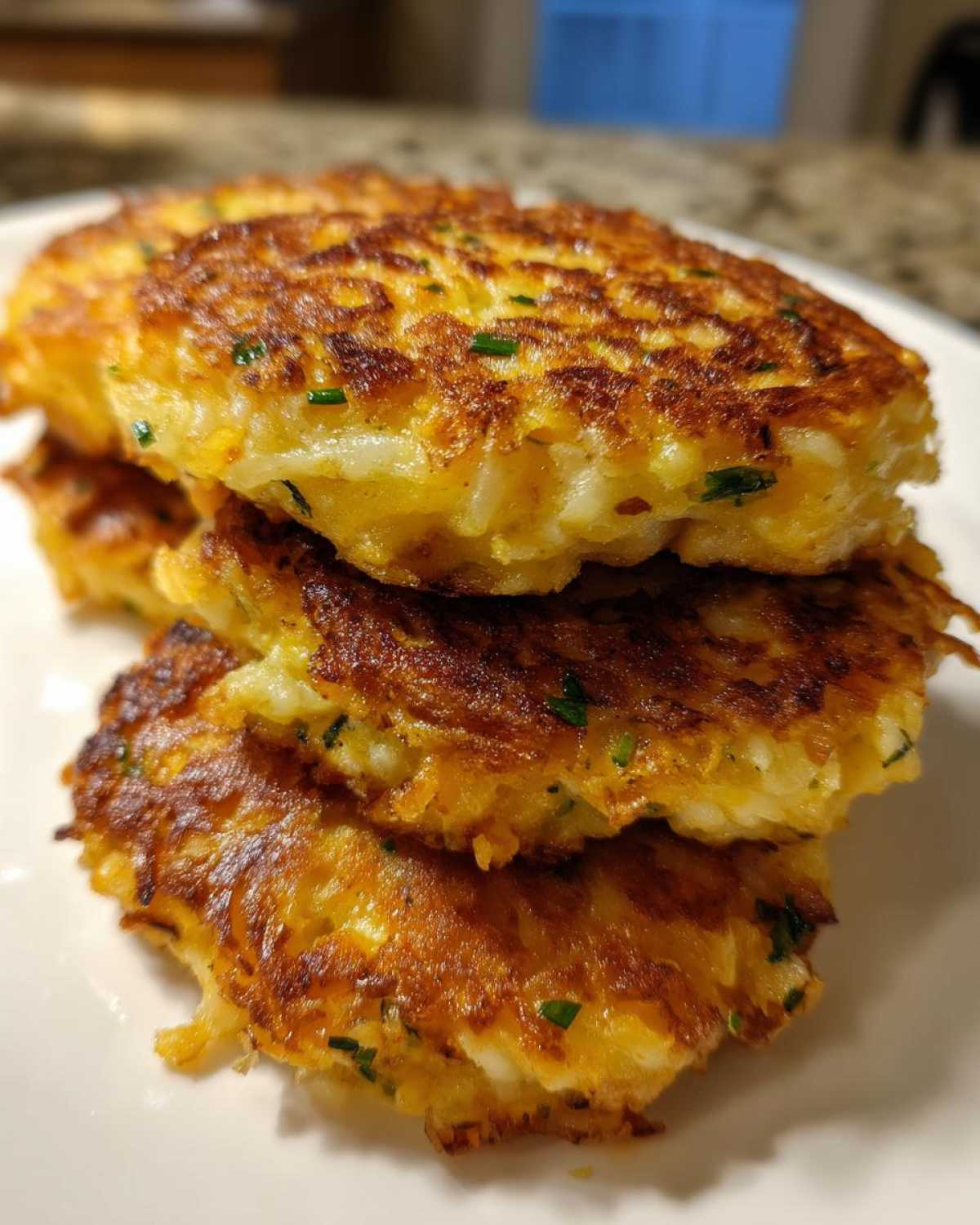 A stack of three golden-brown, crispy mashed potato cakes seasoned with green herbs.