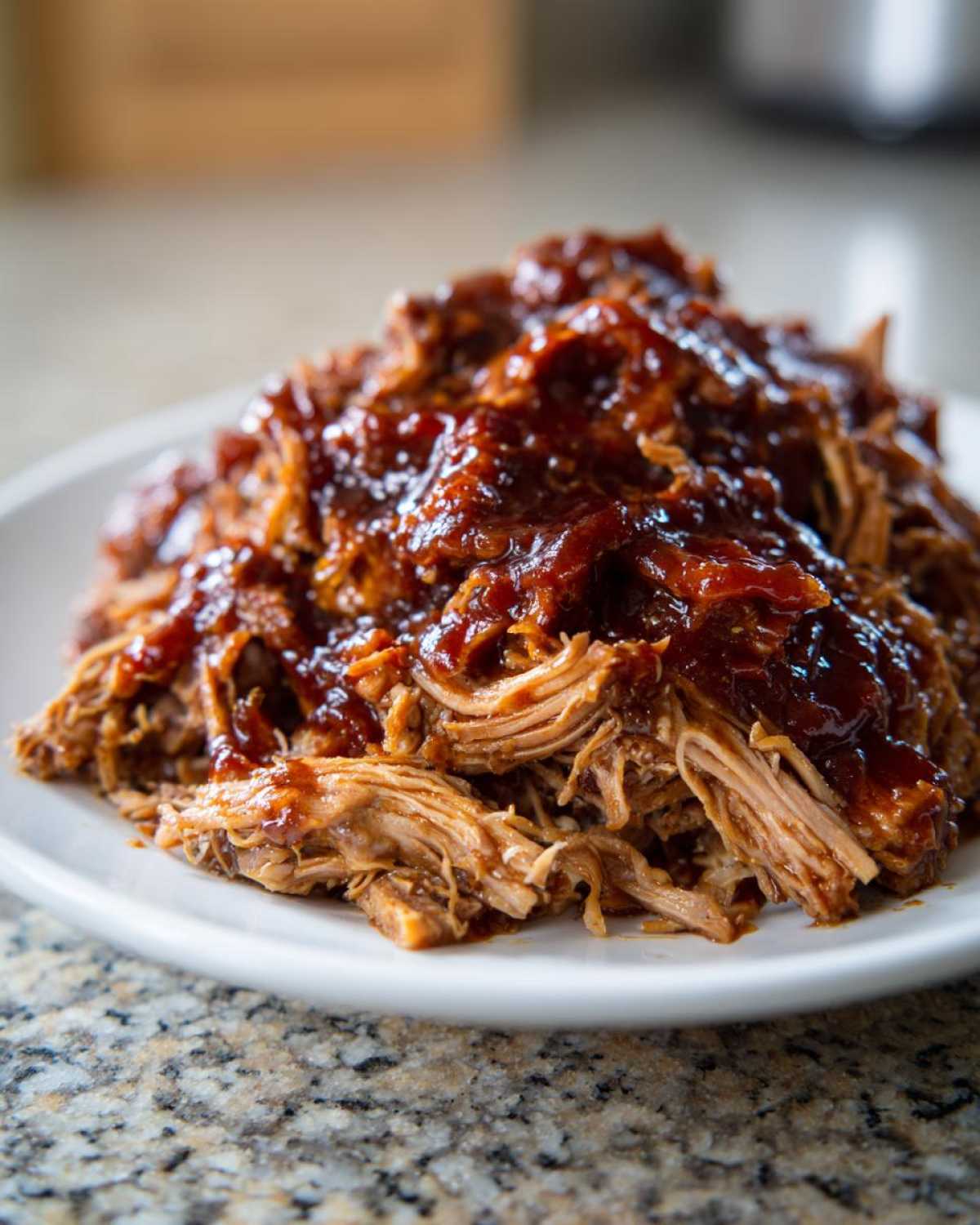 Close-up of tender, shredded crock pot pulled pork generously topped with rich barbecue sauce on a white plate.