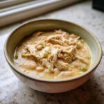 A close-up of a bowl filled with creamy crockpot white chicken chili, featuring shredded chicken and white beans.