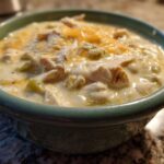 Close-up of a bowl of creamy crockpot white chicken chili topped with melted cheese.