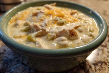 Close-up of a bowl of creamy crockpot white chicken chili topped with melted cheese.