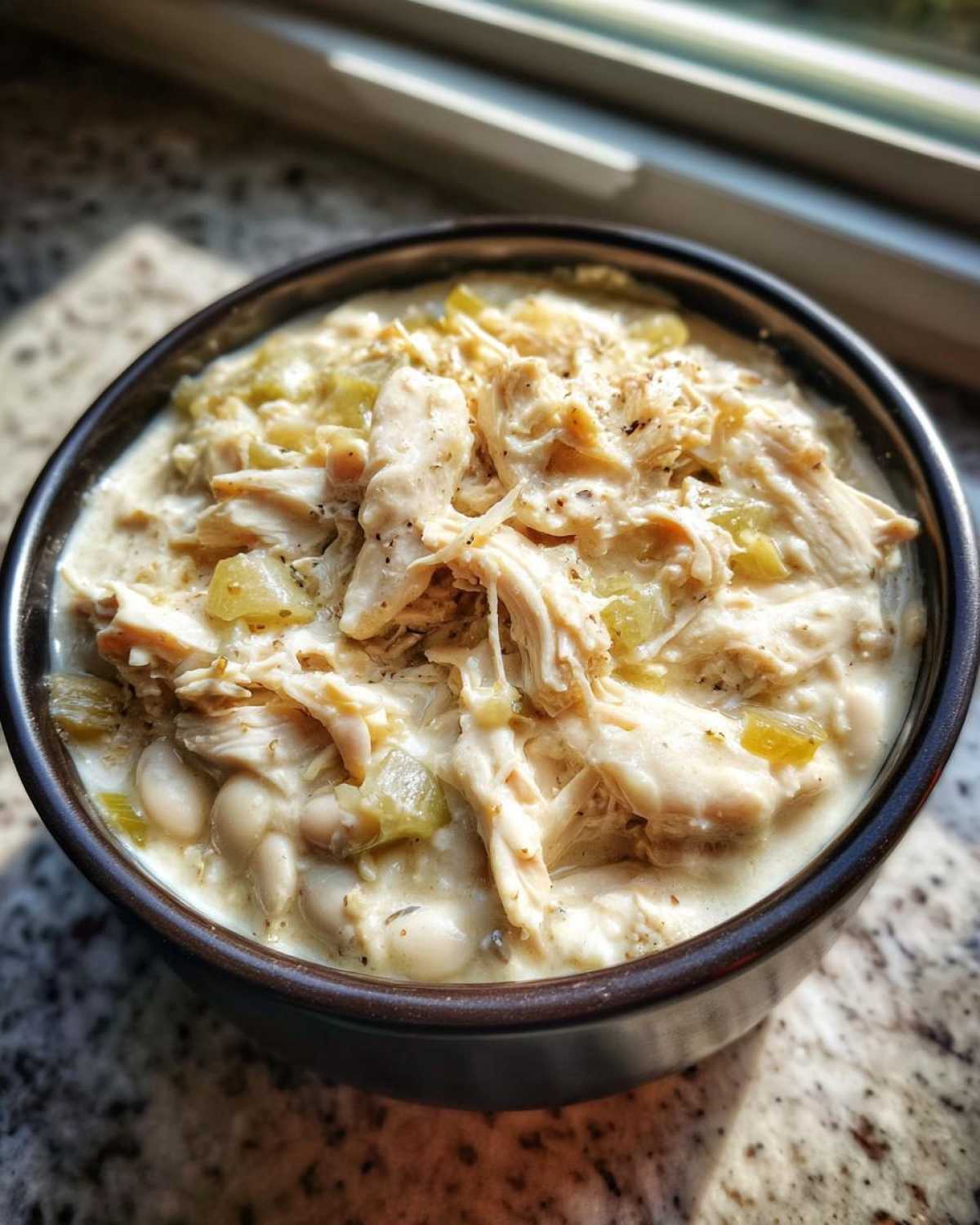 Close-up of a dark bowl filled with creamy crockpot white chicken chili featuring shredded chicken and white beans.