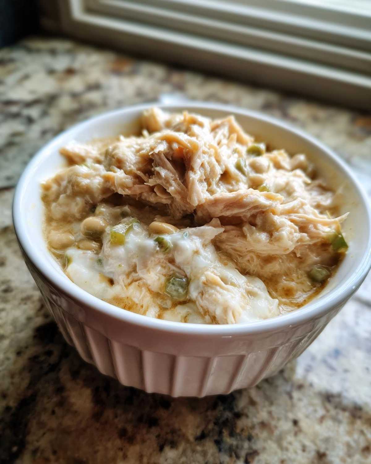 Close-up of a white ramekin filled with shredded chicken and beans from the crockpot white chicken chili.