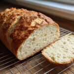A freshly baked loaf of Italian bread, sliced to show the airy crumb, resting on a cooling rack.