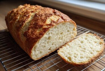 A freshly baked loaf of Italian bread, sliced to show the airy crumb, resting on a cooling rack.
