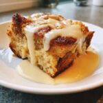 Close-up of a square slice of golden brown bread pudding topped with thick vanilla sauce.