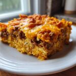 A close-up view of a hearty slice of Dorito Casserole with layers of meat, rice, and melted cheese topping.
