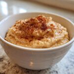 Close-up of creamy homemade applesauce topped generously with ground cinnamon in a white bowl.