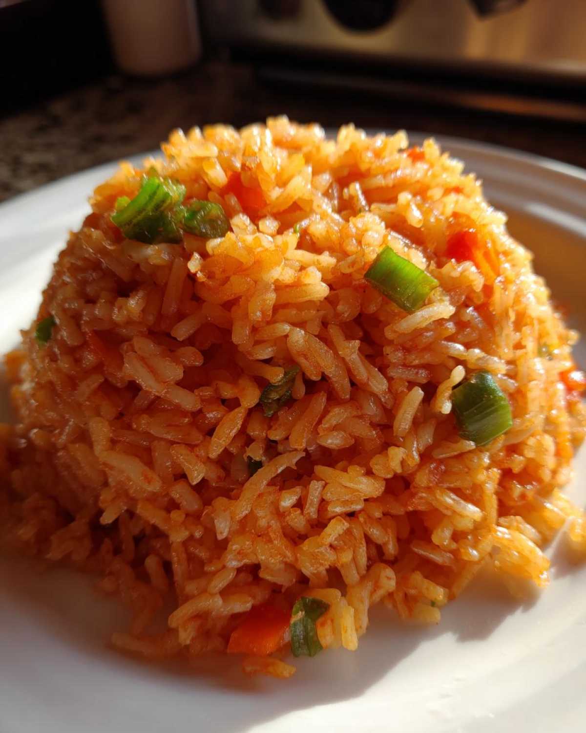A close-up of a perfectly molded mound of bright orange spanish rice garnished with chopped green onions.