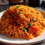 A close-up of a perfectly mounded serving of bright orange Spanish rice garnished with green onions and diced red pepper.