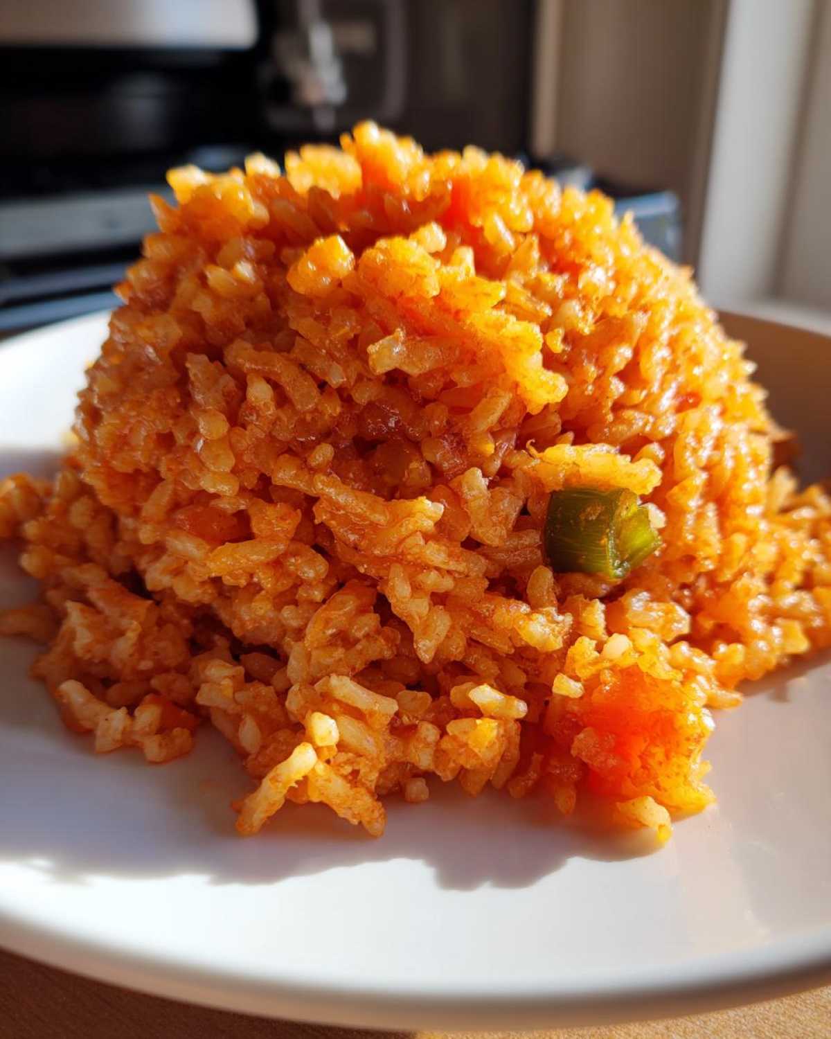 Close-up of a mound of bright orange, seasoned spanish rice served on a white plate, showing texture and a piece of green pepper.