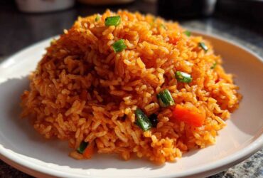 A close-up of a perfectly mounded serving of bright orange Spanish rice garnished with green onions and diced red pepper.