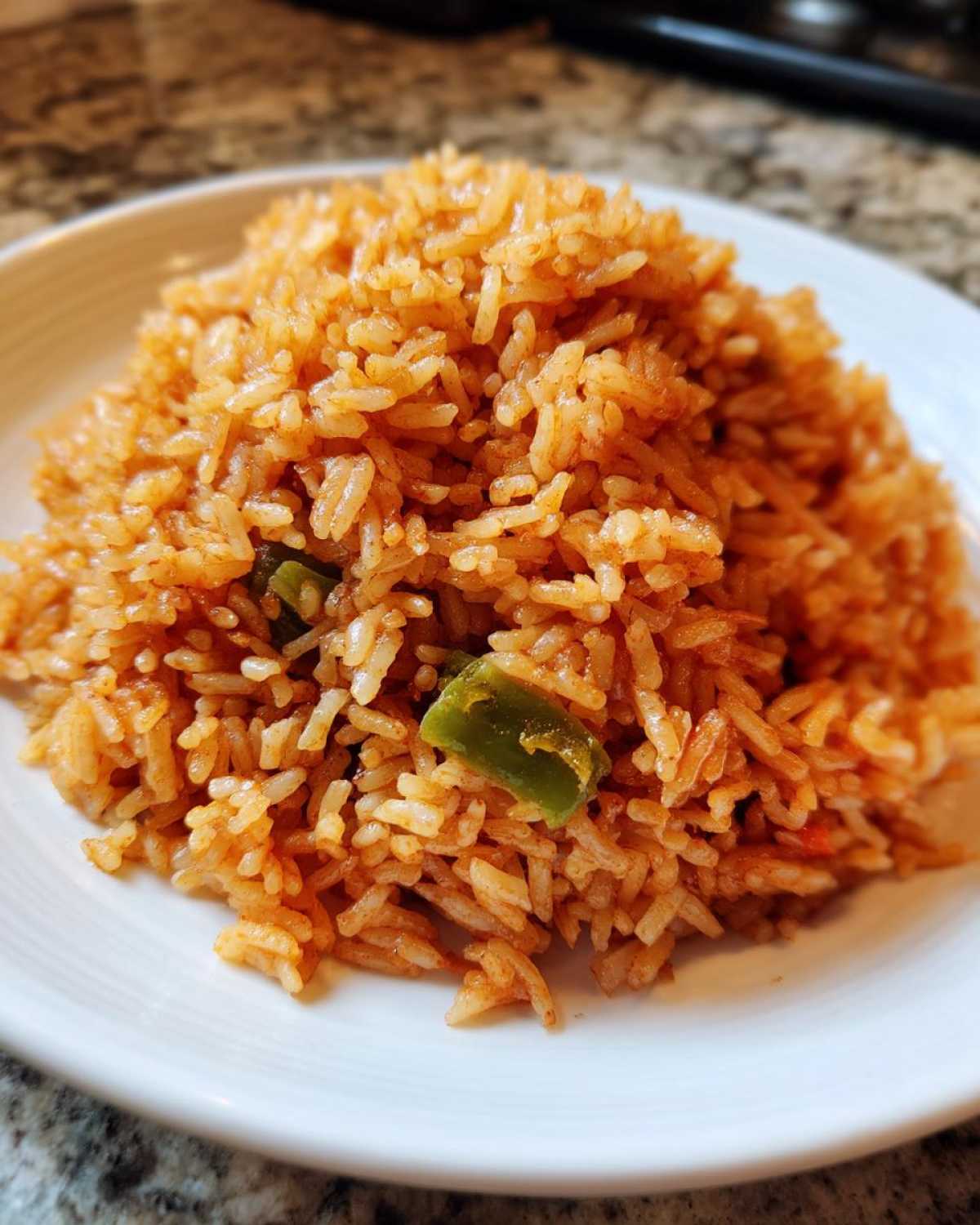 Close-up of a mound of fluffy, orange-red spanish rice with visible pieces of green bell pepper on a white plate.
