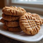 A stack of freshly baked Easy Peanut Butter Cookies showing classic crisscross fork marks on a white plate.