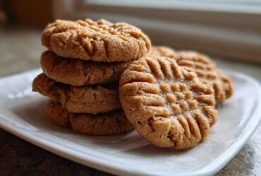 A stack of freshly baked Easy Peanut Butter Cookies showing classic crisscross fork marks on a white plate.