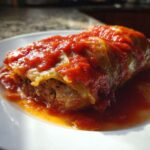 A single serving of savory cabbage rolls smothered in rich tomato sauce, served on a white plate.