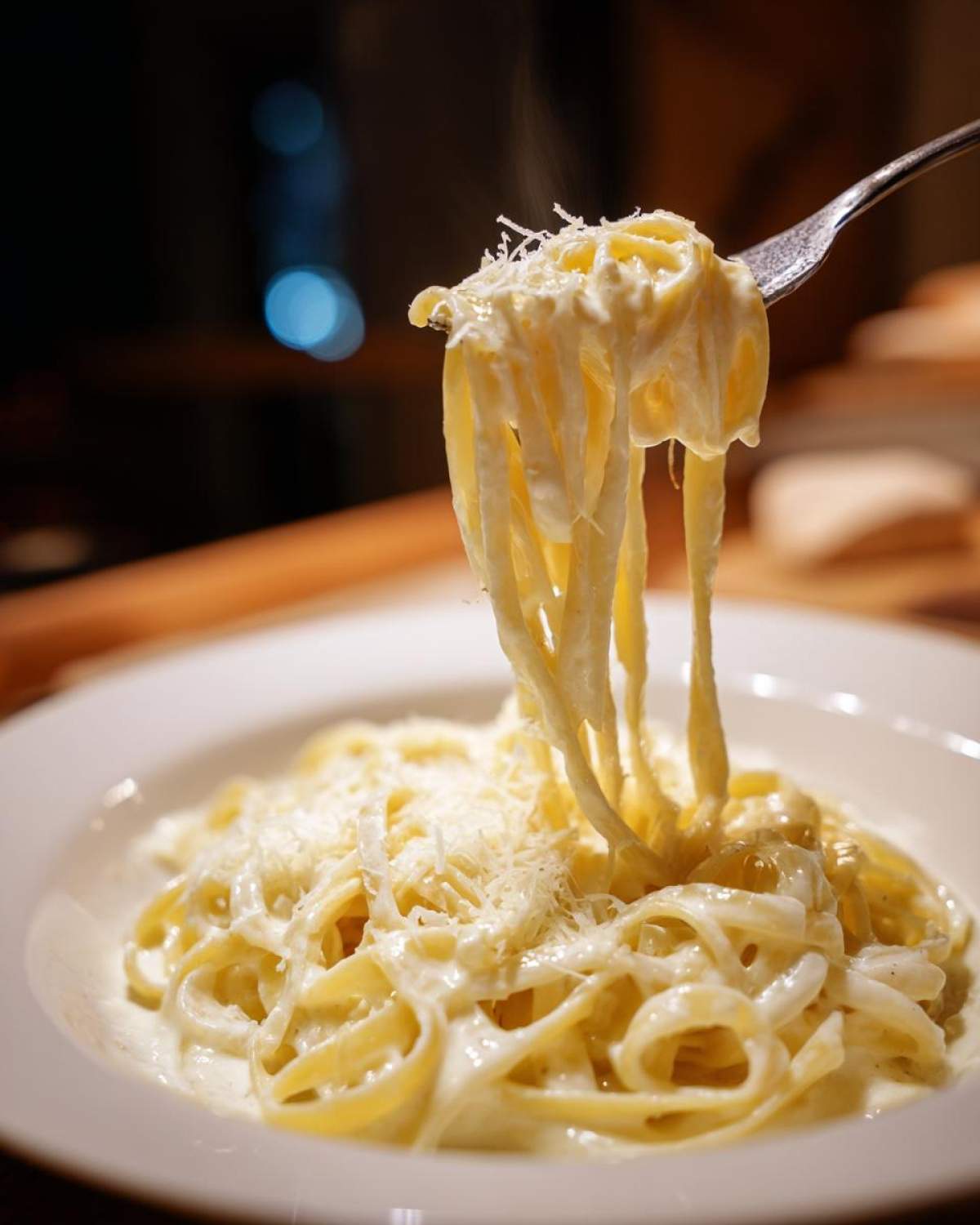 Close-up of fettuccine pasta being lifted by a fork, coated in creamy Olive Garden Alfredo Sauce and topped with grated cheese.