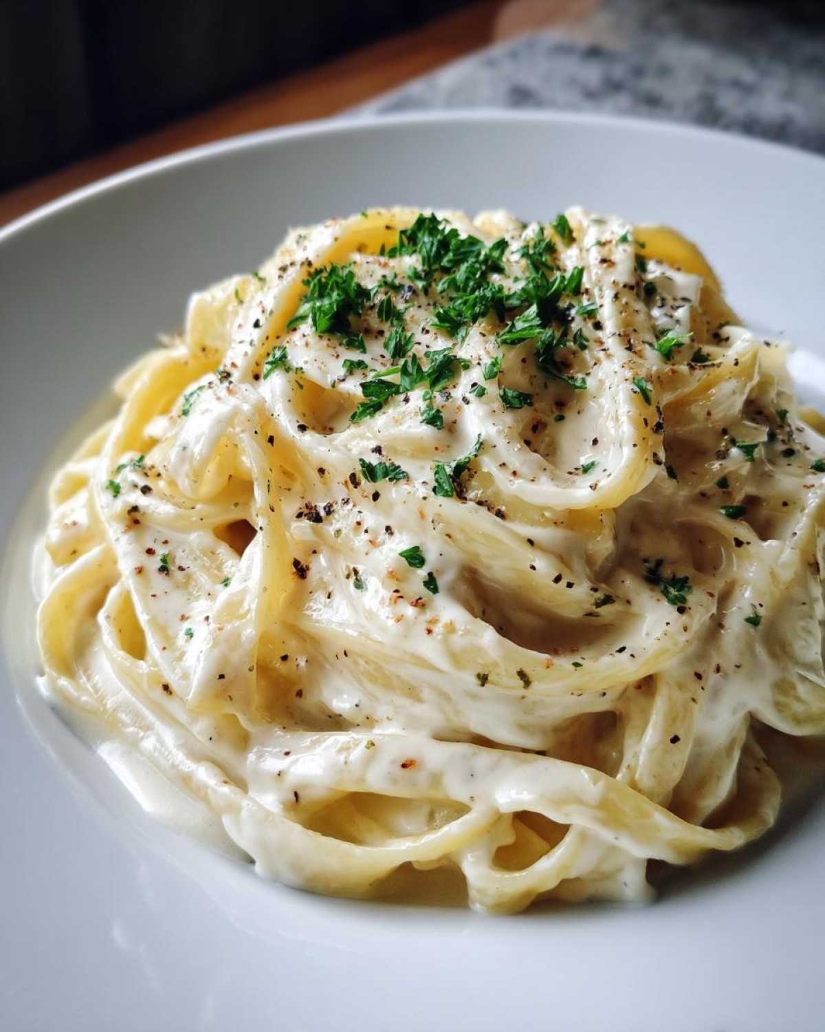 Close-up of fettuccine pasta generously coated in rich homemade alfredo sauce, topped with black pepper and parsley.