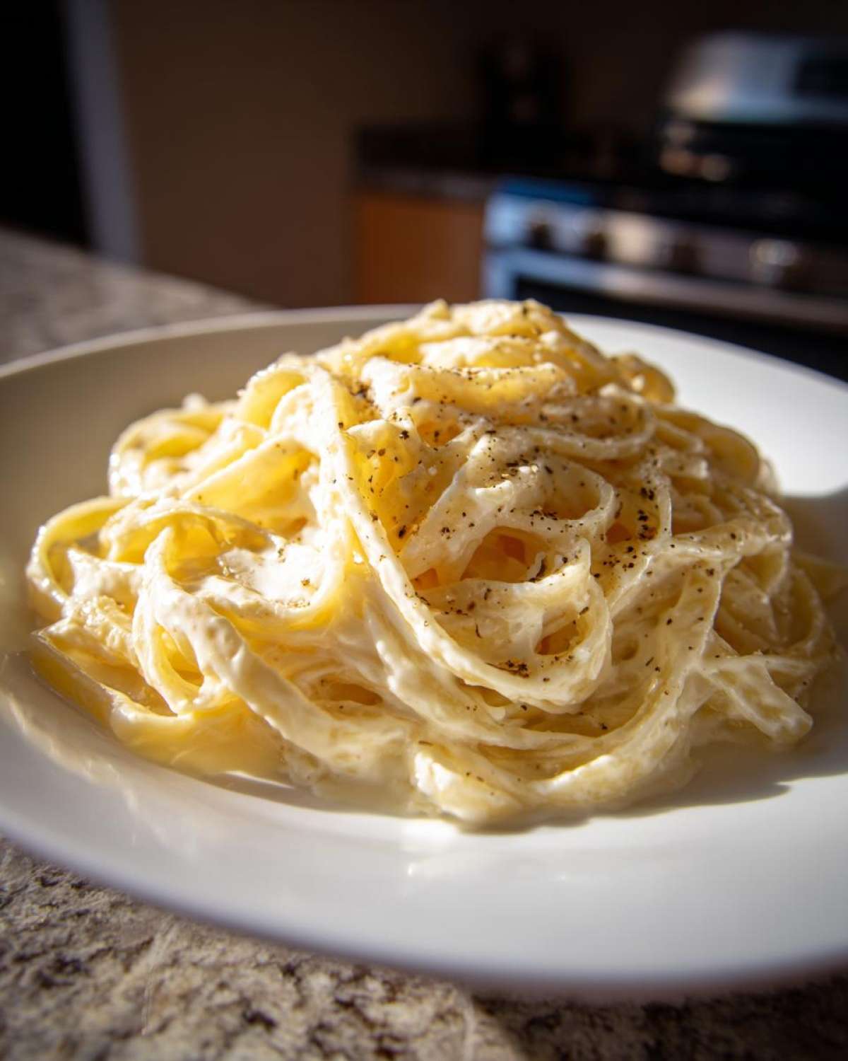 A close-up of fettuccine pasta generously coated in creamy homemade alfredo sauce and topped with black pepper.