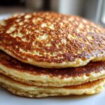 Close-up of a fluffy stack of golden brown almond flour pancakes showing perfect air bubbles.
