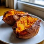 Two fluffy baked sweet potatoes, split open to show the bright orange interior, served on a white plate.