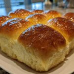 Close-up of a batch of golden brown, glossy dinner rolls brushed with butter.
