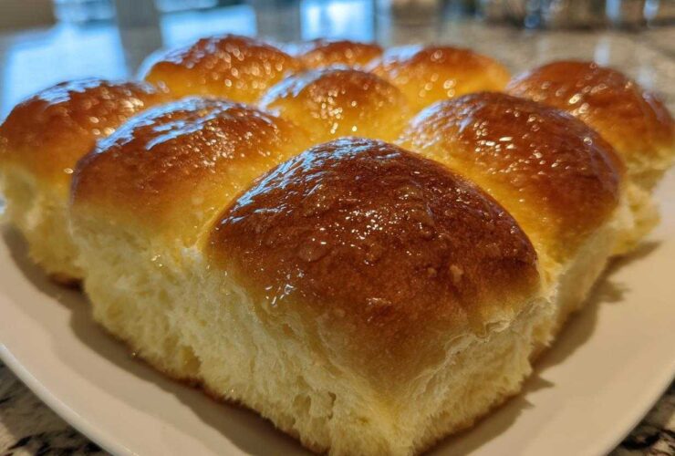 Close-up of a batch of golden brown, glossy dinner rolls brushed with butter.