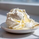 A generous mound of fluffy, white cream cheese frosting sits in a small white bowl, ready to use.