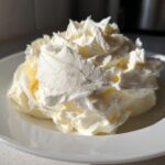 A large, fluffy swirl of homemade cream cheese frosting piled high on a white plate, ready for use.