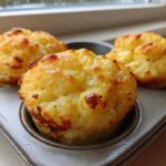 Three golden brown, fluffy muffin tin egg bites sitting in a metal muffin pan near a window.