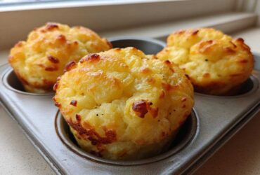 Three golden brown, fluffy muffin tin egg bites sitting in a metal muffin pan near a window.