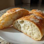 A loaf of golden-crusted french bread sliced in half, showing a soft, airy interior crumb.