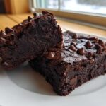 Two fudgy black bean brownies topped with melted chocolate chips served on a white plate.