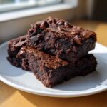 Two fudgy black bean brownies stacked on a white plate, topped with melted chocolate chips.