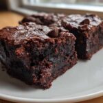 Close-up of two rich, dark, fudgy sweet potato brownies topped with chocolate chips on a white plate.