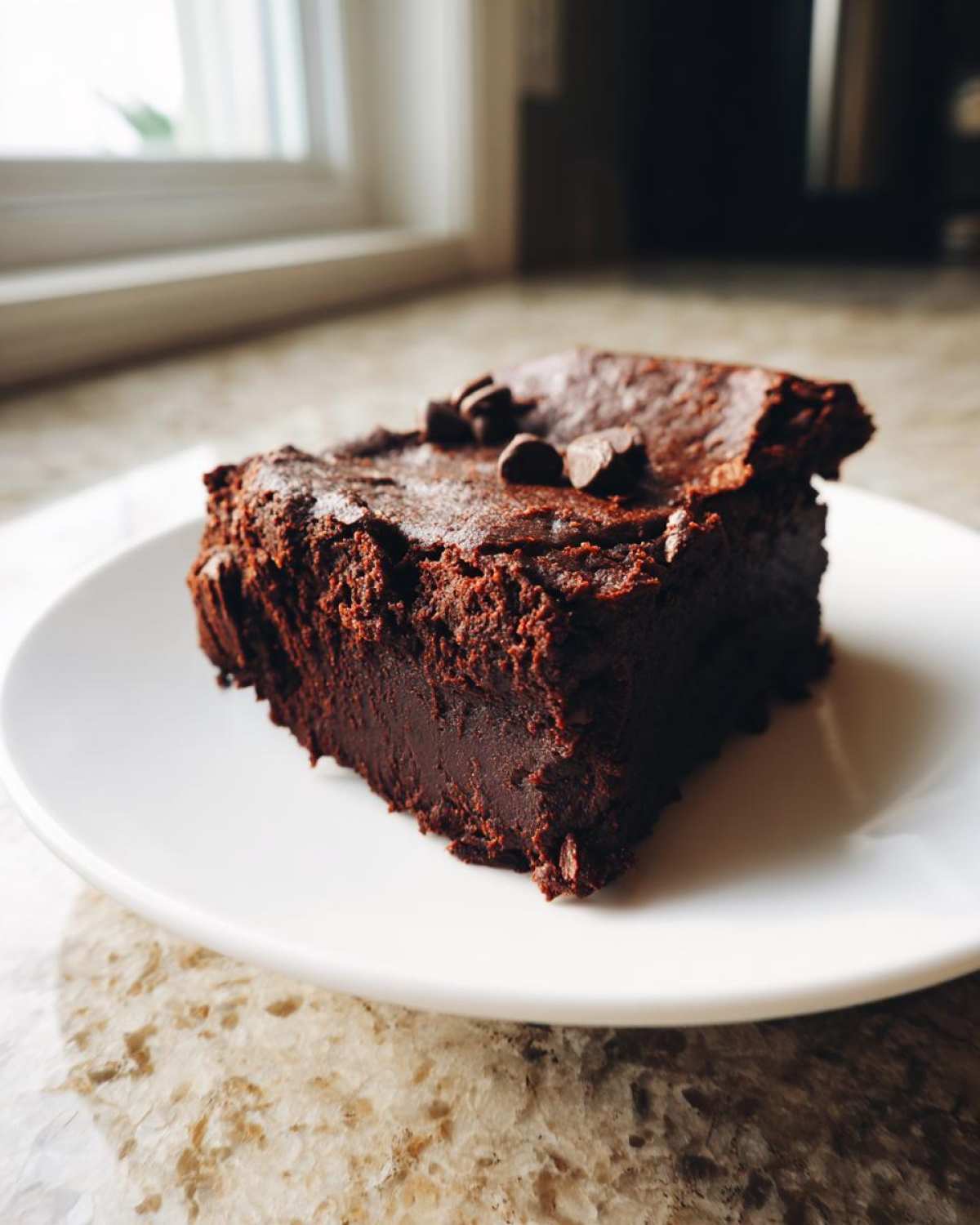 A close-up of a single, thick, fudgy square of sweet potato brownies topped with chocolate chips.