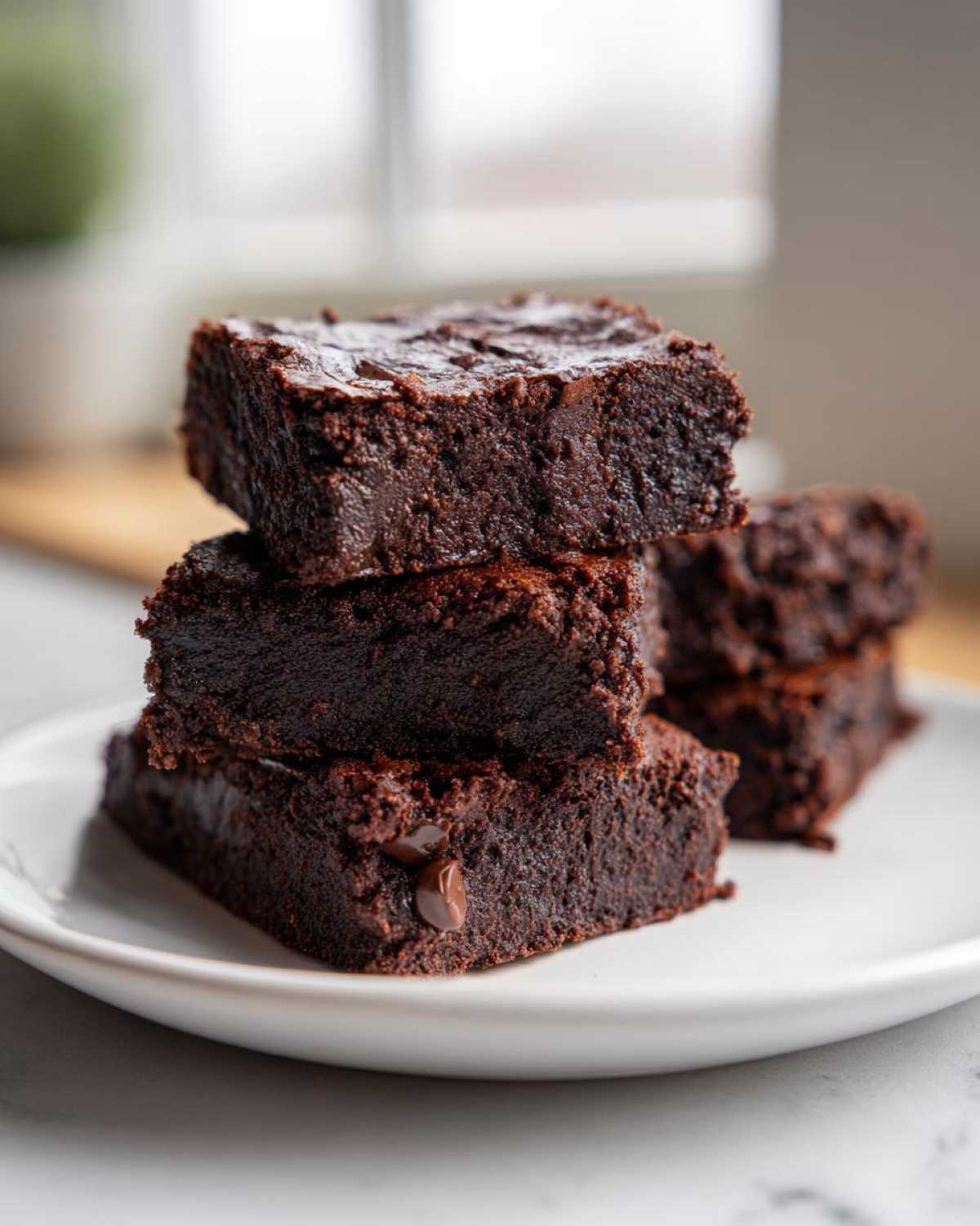 A stack of four rich, fudgy sweet potato brownies piled on a white plate.