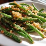 Close-up of bright green beans tossed with crispy, golden garlic parmesan topping on a white plate.