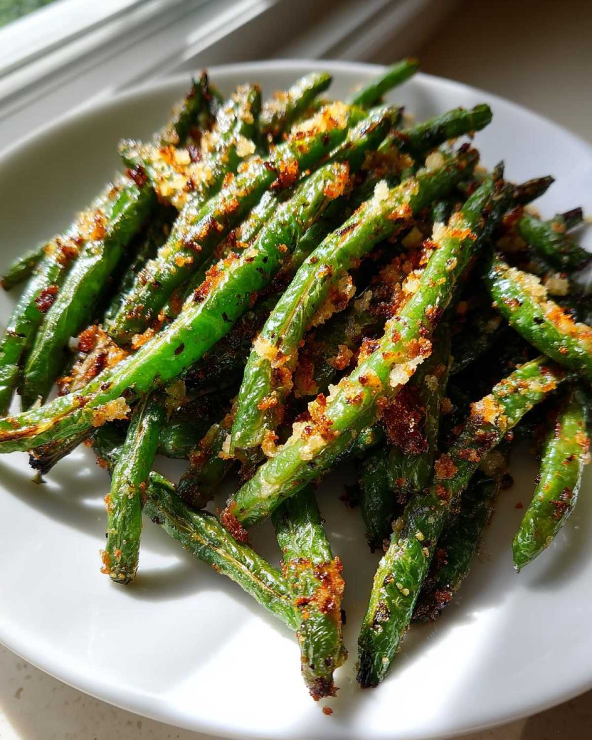 Close-up of bright green beans coated in crispy, golden brown garlic parmesan topping served on a white plate.