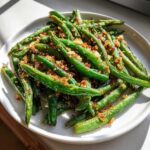 Bright green beans tossed with crispy garlic parmesan topping served on a white plate.
