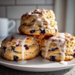 A stack of three fluffy blueberry scones generously topped with a thick white glaze, ready to eat.