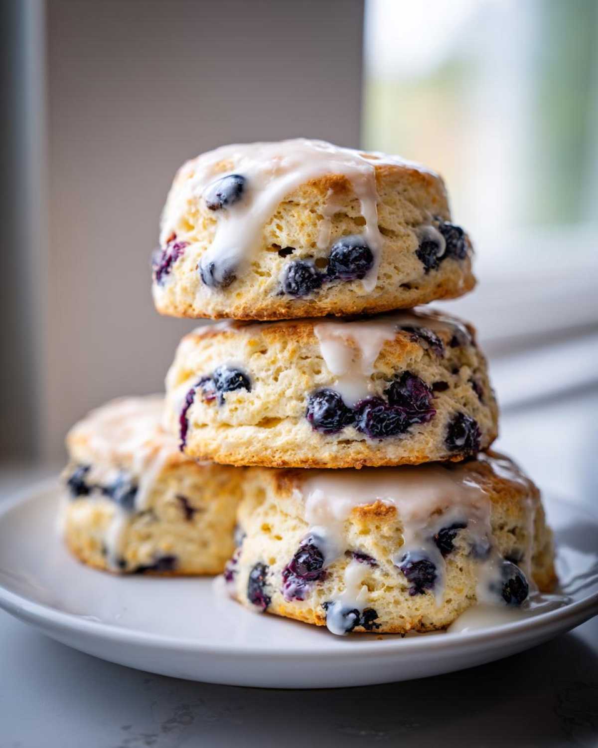 Three stacked, freshly baked blueberry scones topped with a thick white glaze.