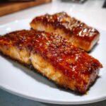Two perfectly cooked salmon steaks covered in a thick, shiny, caramelized glaze on a white plate.