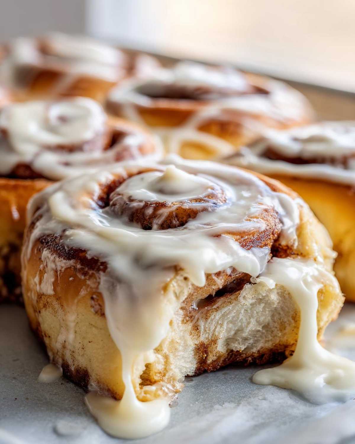 A close-up shot of a soft, freshly baked cinnamon roll with thick, dripping cream cheese frosting.