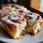 A close-up of a soft, gooey cinnamon roll with thick white icing, one piece pulled away to show the fluffy interior.