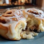 A close-up of a soft, fluffy cinnamon roll broken open, covered in thick white icing.
