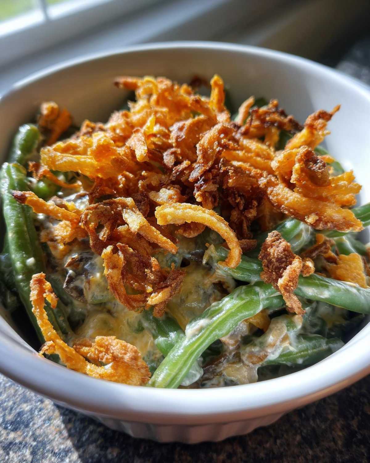 Close-up of a white bowl filled with creamy green bean casserole topped generously with crispy fried onions.