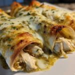 Close-up of three baked green chile chicken enchiladas covered in melted white cheese and green chile sauce.